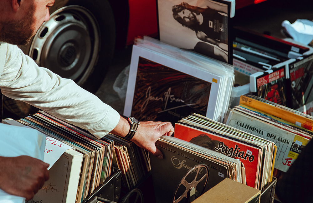 Bakluckeloppis där backar är fyllda med vinylskivor. En man med vit skjorta sträcker fram sin hand för att leta bland vinylskivorna.