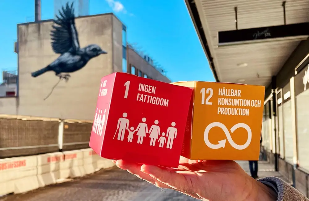 Ett år med globala målen. Bilden visar två kuber med de globala målen Ingen fattigdom (mål 1) och Hållbar Konsumtion (mål 12) framför en väggmålning föreställande en svart fågel i Nässjö.