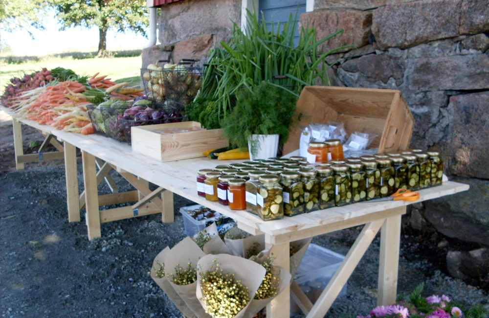 Ett träbord utomhus med grönsaker, blommor och glasburkar med inlagd gurka.