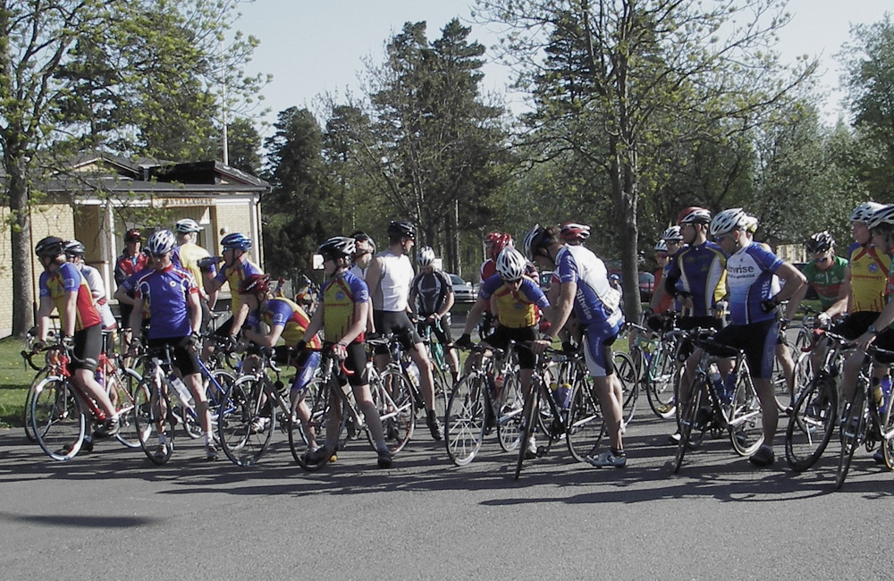Cyklister som samlats och står uppradade på asfaltsväg.