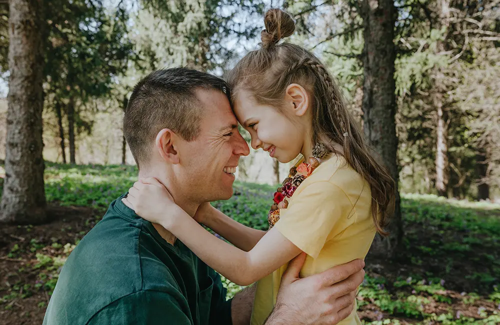 En
leende man i grön t-shirt och en glad flicka i gul t-shirt står nära varandra
utomhus i solsken, med pannorna mot varandra i en kärleksfull pose. Tillsammans
bildar deras huvuden och flickans arm formen av ett hjärta.