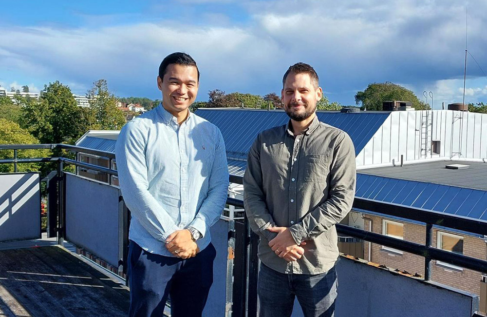 Mehdi Jan och Johan Putsén står på en terrass i solsken med byggnader i bakgrunden.