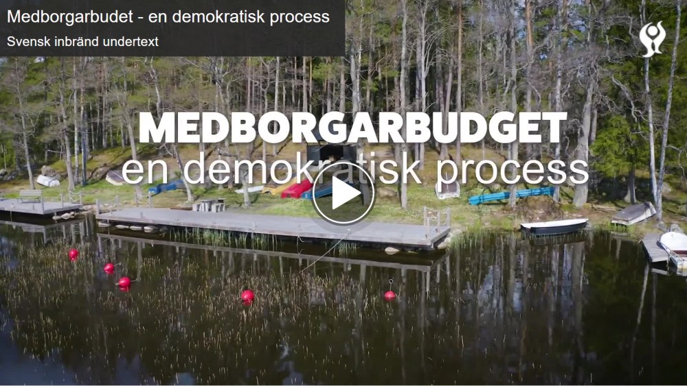 Bild som visar en videospelare med texten medborgarbudget - en demokratisk process. I bakgrunden är det en sjö med brygga, båtar och skog.