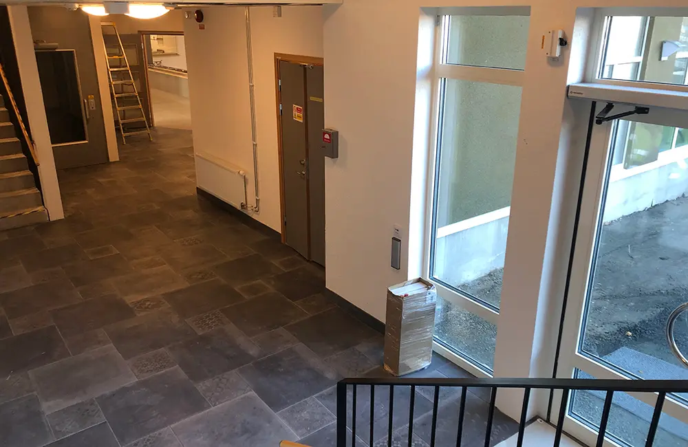 Inomhusmiljö med trappa, grå golv, en dörr och fönster.