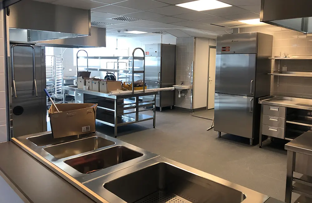 Inomhusmiljö med matlagningskök, plastgolv och fönster.