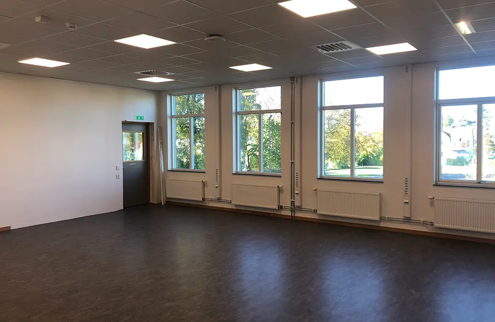 Inomhusmiljö med mörkt golv, belysning i taket och fönster.