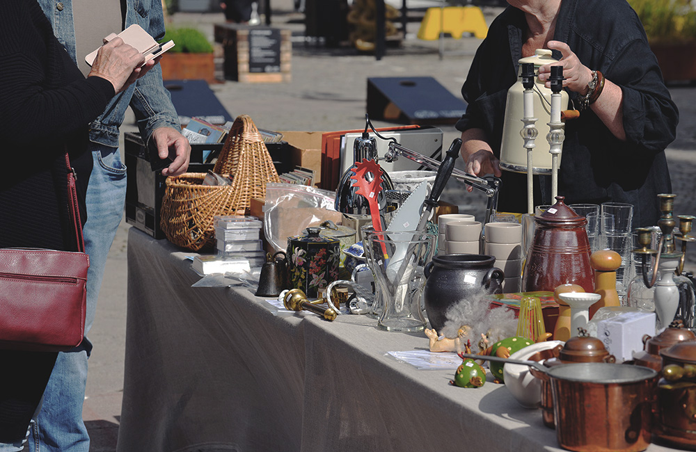 På torget i Nässjö står ett bord fyllt med loppisprylar. Bakom bordet står en säljare och framför två kunder.