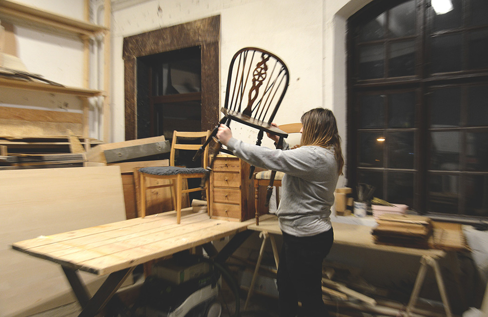 Magdalena står i verkstaden och visar upp en pinnstol som hon ska reparera.