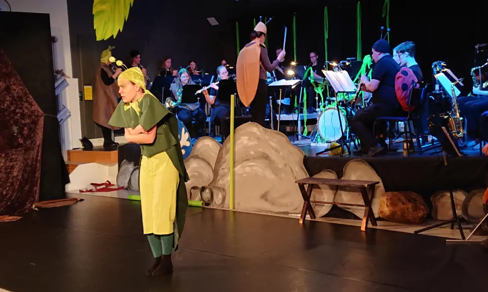 I bakgrunden sitter
orkestern på scenen och spelar. Framför scenen står "syrsan" och
fryser.
