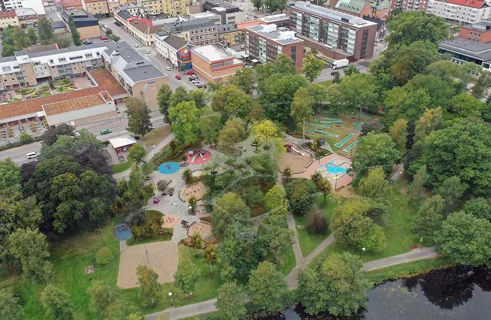 Flygbild över Stadsparken i Nässjö. På bilden syns en färgglad lekplats, bostadshus, gröna träd och en sjö.