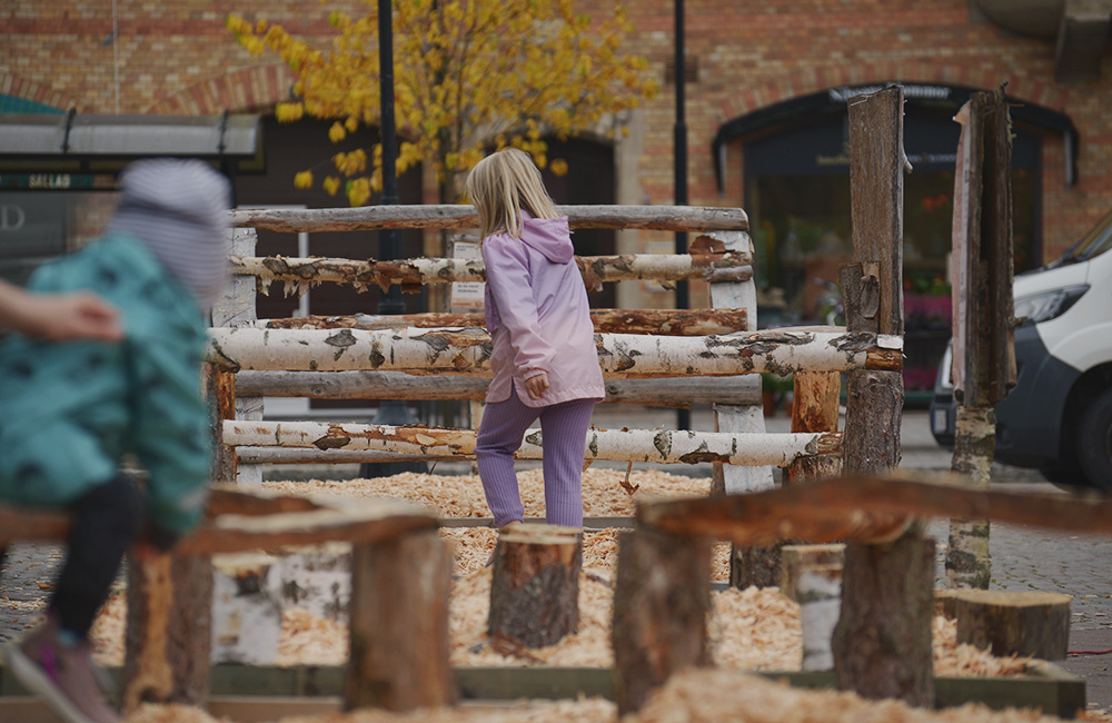 Flicka i lila kläder hoppar över en hinderbana gjord av stockar och stubbar.