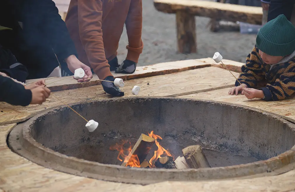 Tre personer står runt en eld och grillar marshmallows