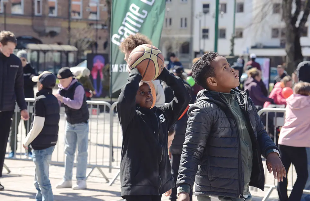 Barn står med basketbollar och försöker pricka basketkorgen. 