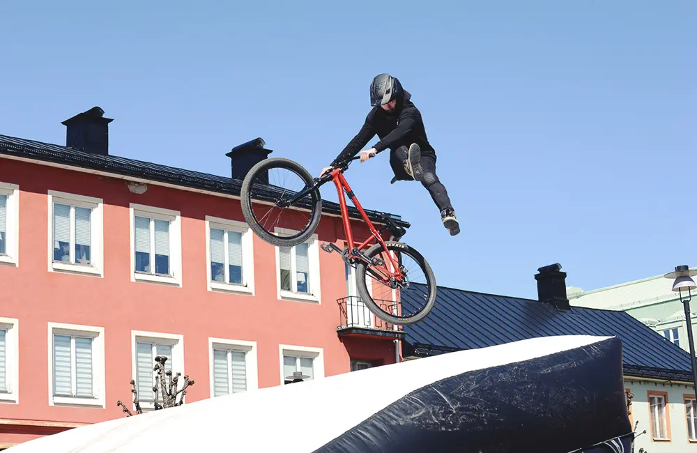 En MTB-cykel är i luften. Cyklisten gör trix i luften innan han landar på en stor uppblåsbar kudde.