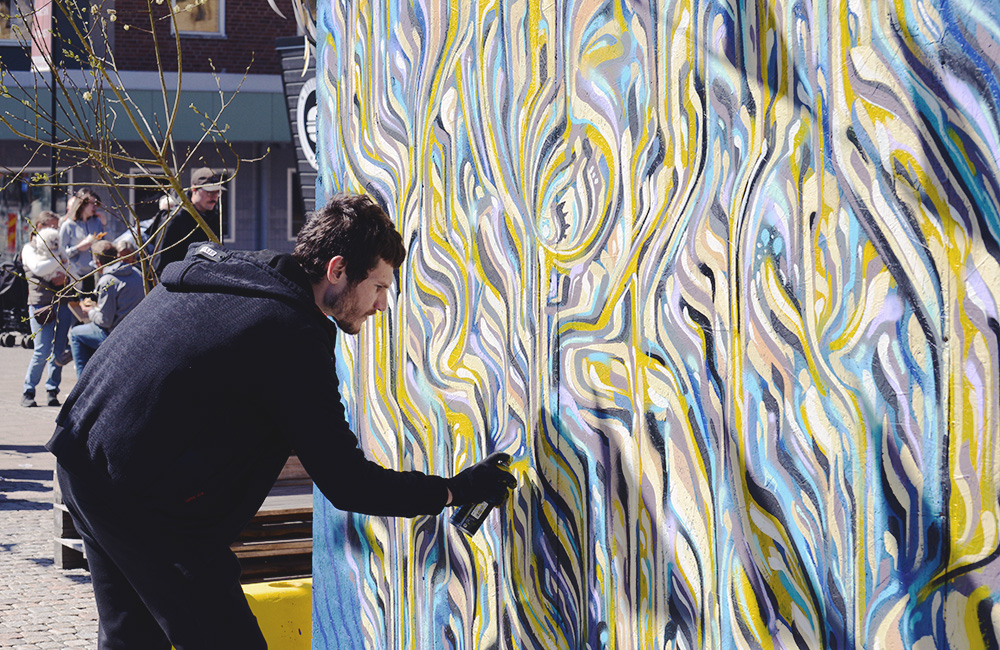 En man står och målar en väggmålning i färgstarka kulörer. 