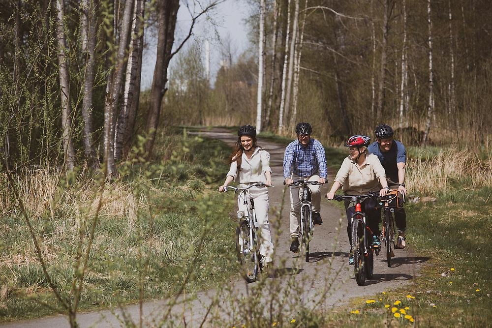 En solig vårdag där fyra personer cyklar på en grusväg i skogen.