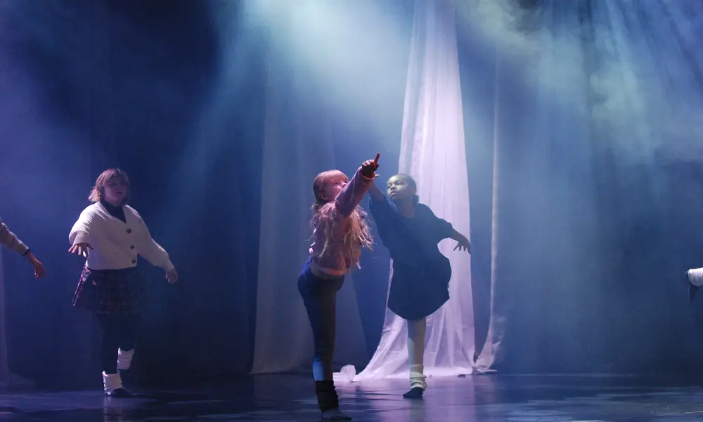 Tre dansare på scenen. Samtliga står på ett ben och pekar upp mot taket. I bakgrunden hänger en vit slöja. Scenen är lite vackert rökig.