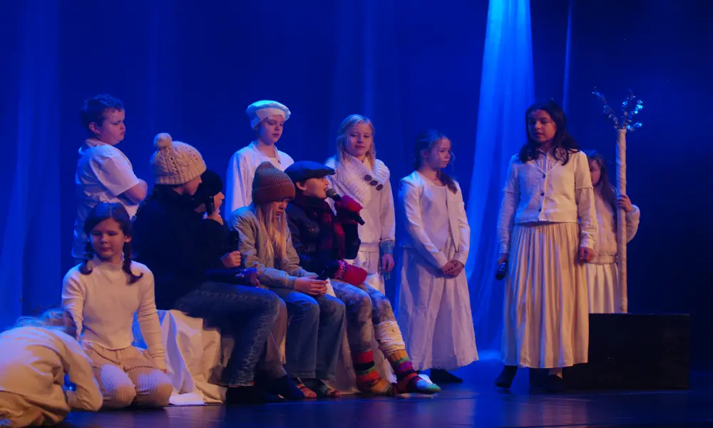 Ett helt gäng barn är samlade på scenen. Några iklädda vinterkläder, andra vita dräkter.