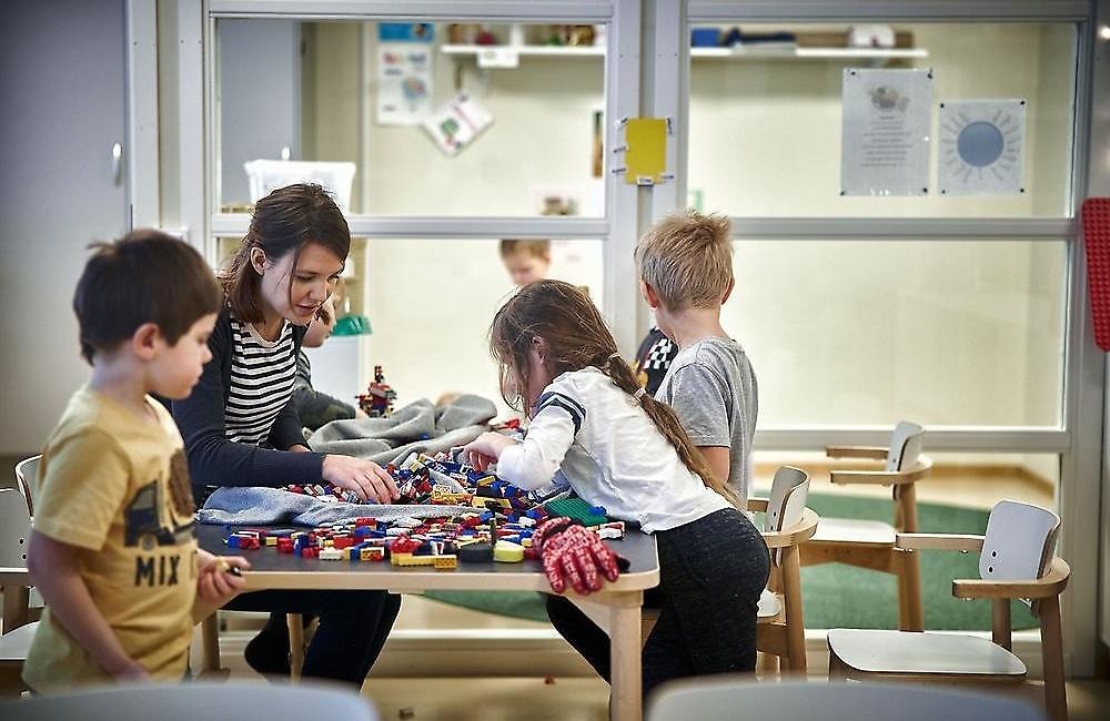 Förskollärare med tre barn som tillsammans bygger med lego på ett bord.
