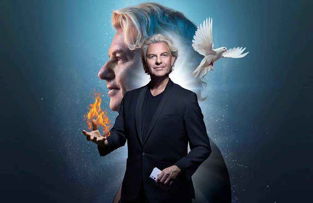 Magikern Joe Labero i svart kostym. Han håller ett seplkort i ena handen och en eldflamma i andra. Vid hans axel flyger en vit duva och i bakgrunden är hans ansikte i profil. Bakgrunden är blå och svart.