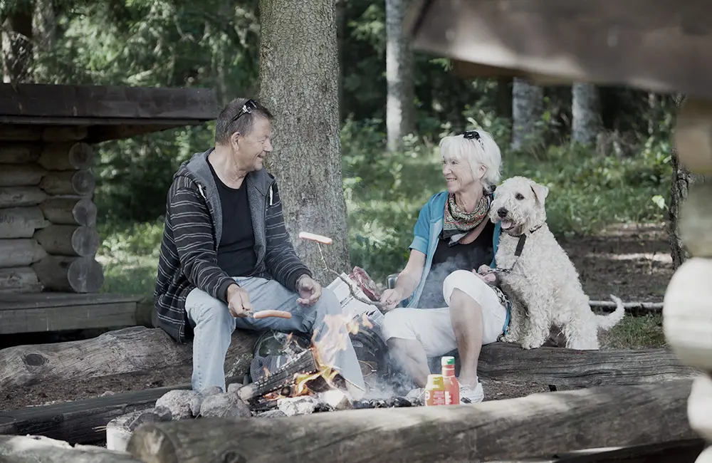 En man  och en kvinna med en hund, grillar korv vid vindskydd.