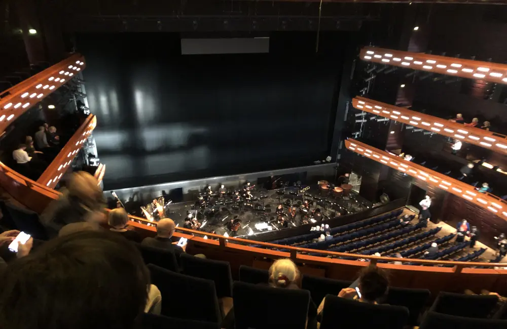 Bilden visar en teatersalong. Man ser scenen lång därframme. Det är vacker belysning längs balkongerna.