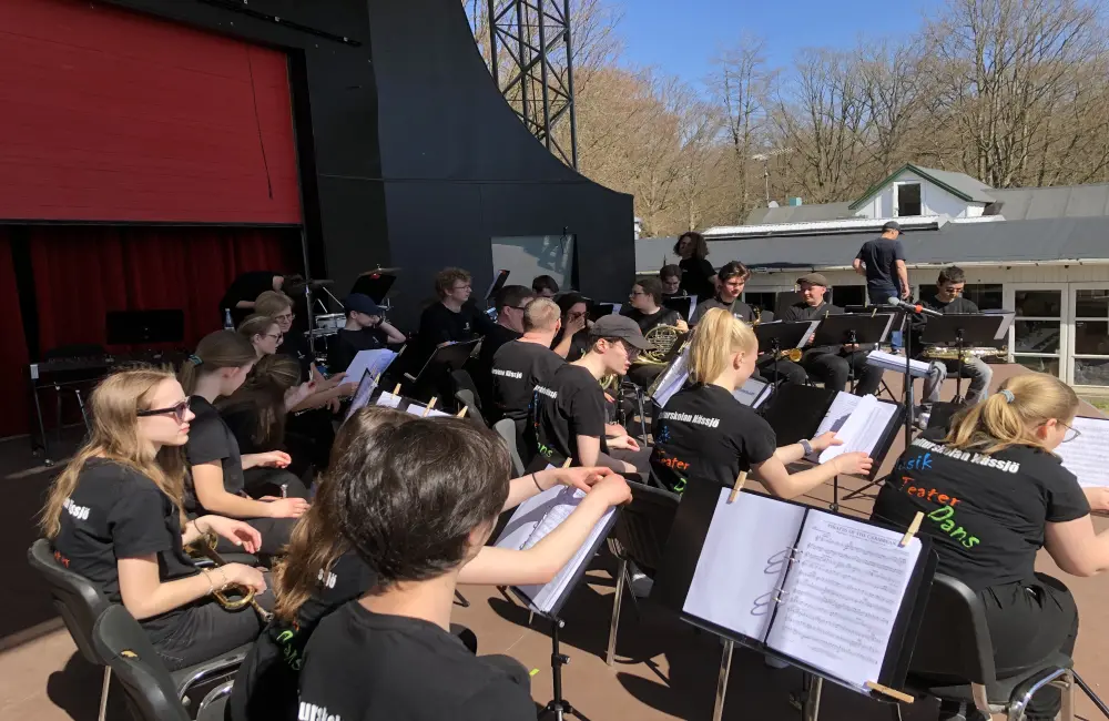 En orkester bestående av ungdomar sitter på en scen, redo att snart börja spela.