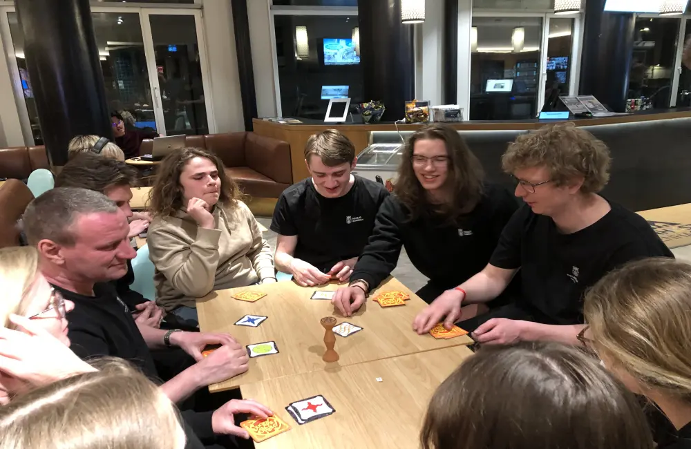 En grupp ungdomar och deras lärare sitter och spelar spel tillsammans.