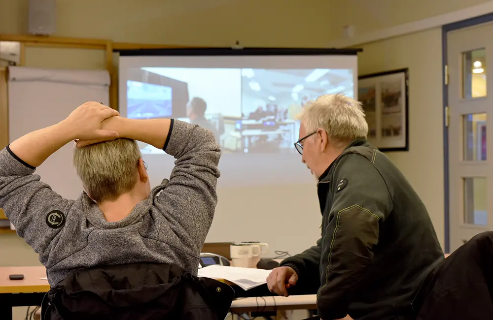 Två lokförare som sitter framför en projektduk i ett klassrum och samtalar.