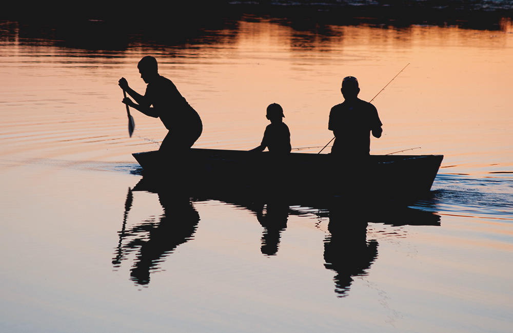 Tre personer fiskar från en roddbåt i solnedgången