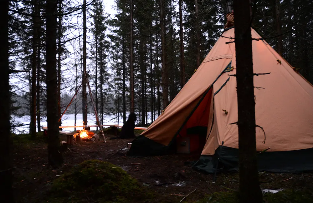 Lägereld och tipitält i skogen