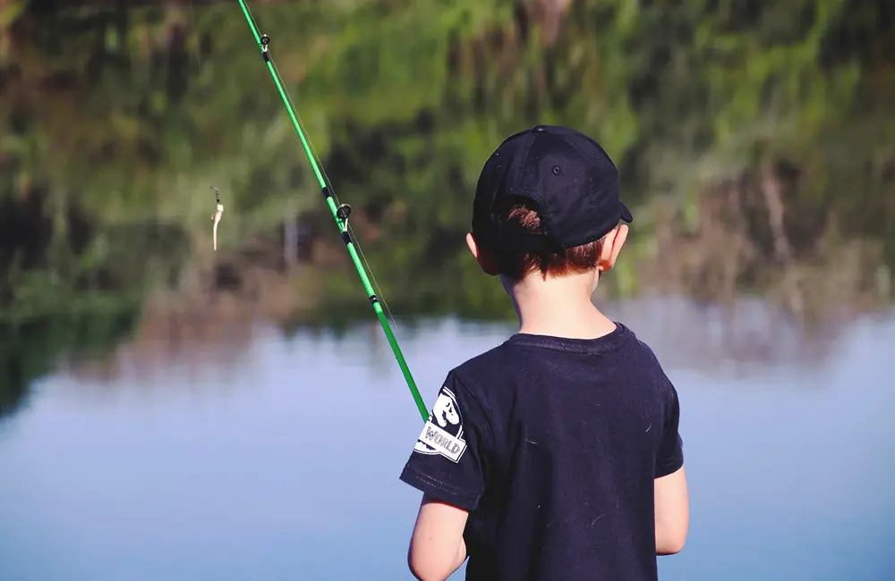 Liten pojke står och fiskar