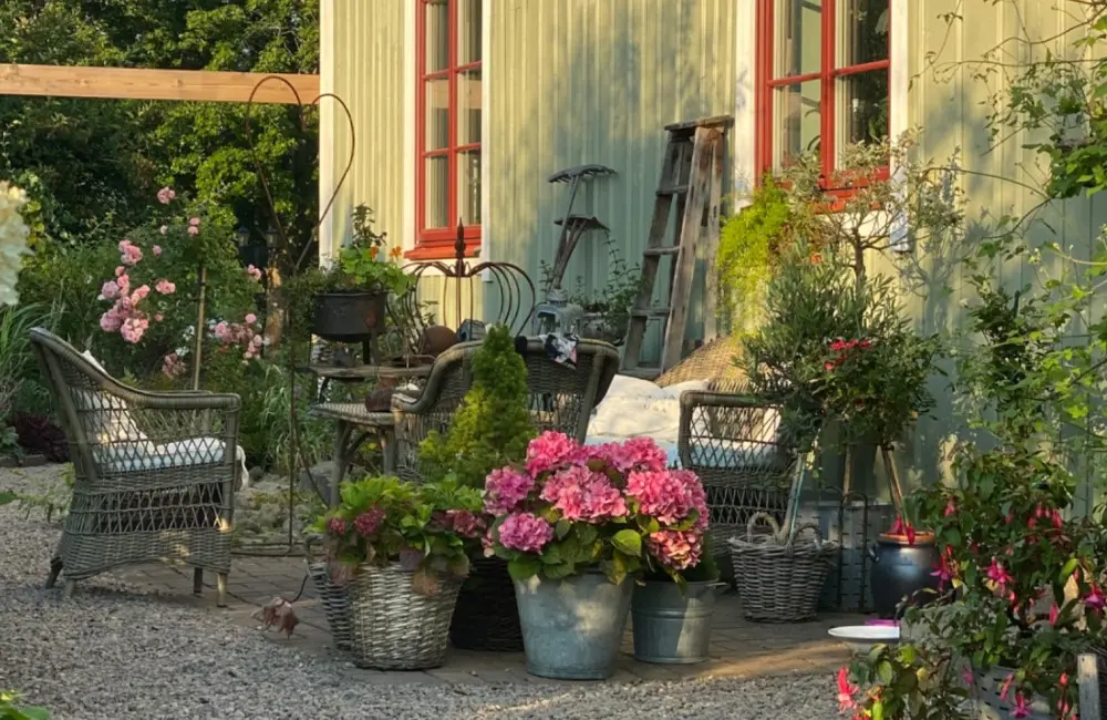 Ett hus och en grusgång med blomplanteringar och trädgårdsmöbler.