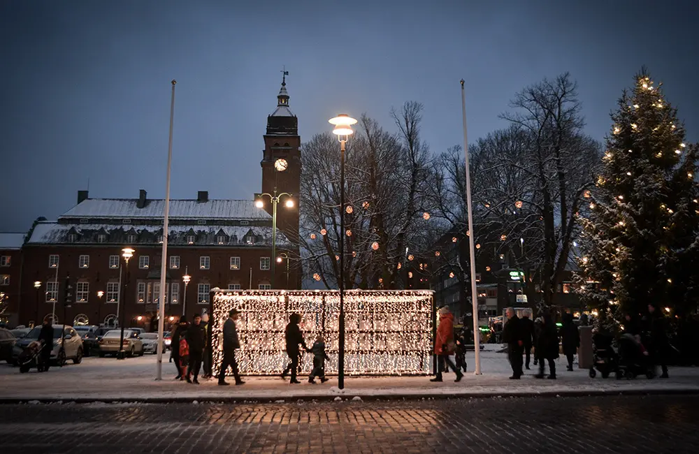 Stortorget i Nässjö med stadshuset i bakgrunden och en stor gran med lampor. På torget står en ljustunnel med några människor som går framför. Det är mörkt och lamporna lyset upp torget.