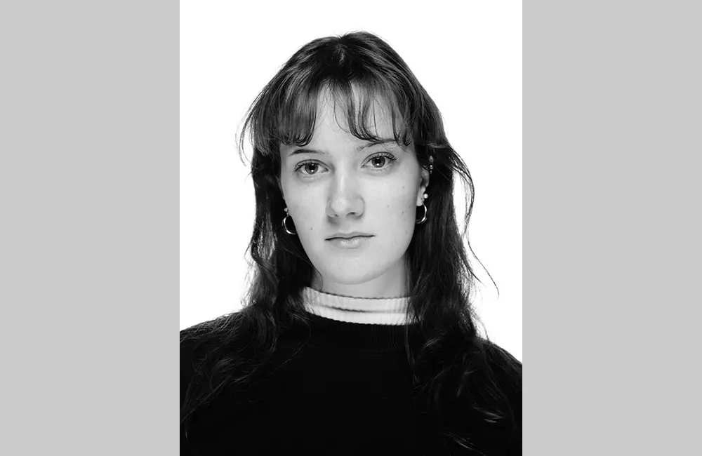 Svartvit porträttbild på Mimmi som har en mörk tröja, ljus polokrage, lugg, samt hår som går ner över axlarna.