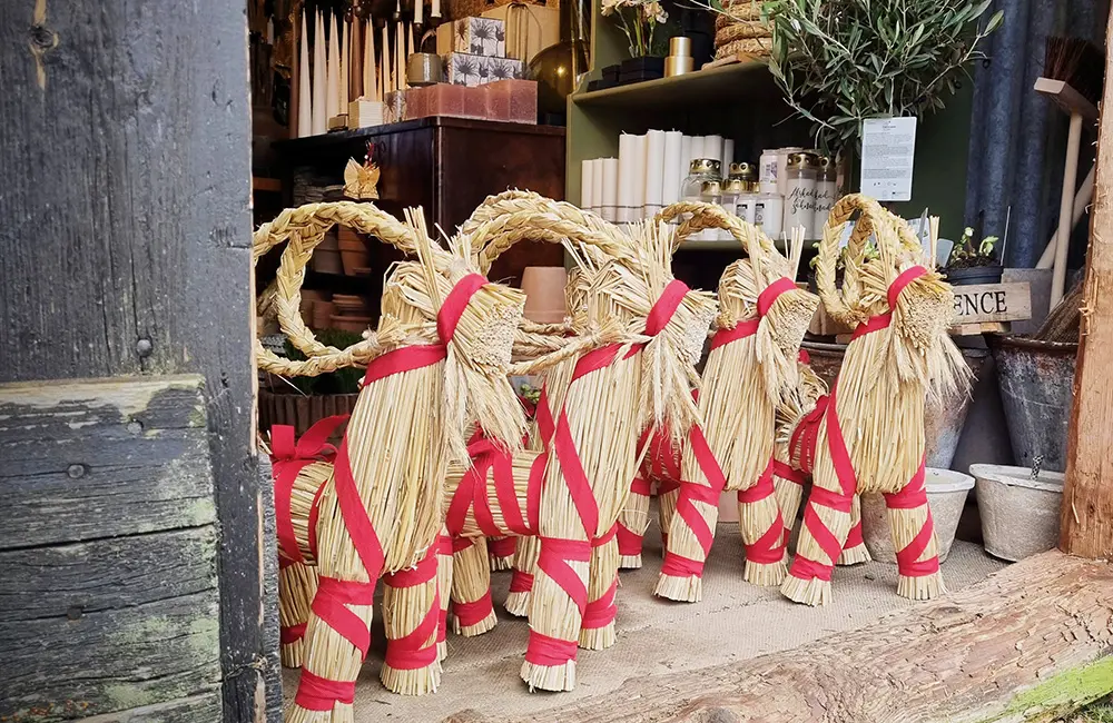 Fyra julbockar i halm står i en dörröppning. Bakom är det hyllor med ljus och pynt.