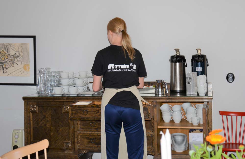 Feriepraktikant som ställer fram koppar på en bänk.