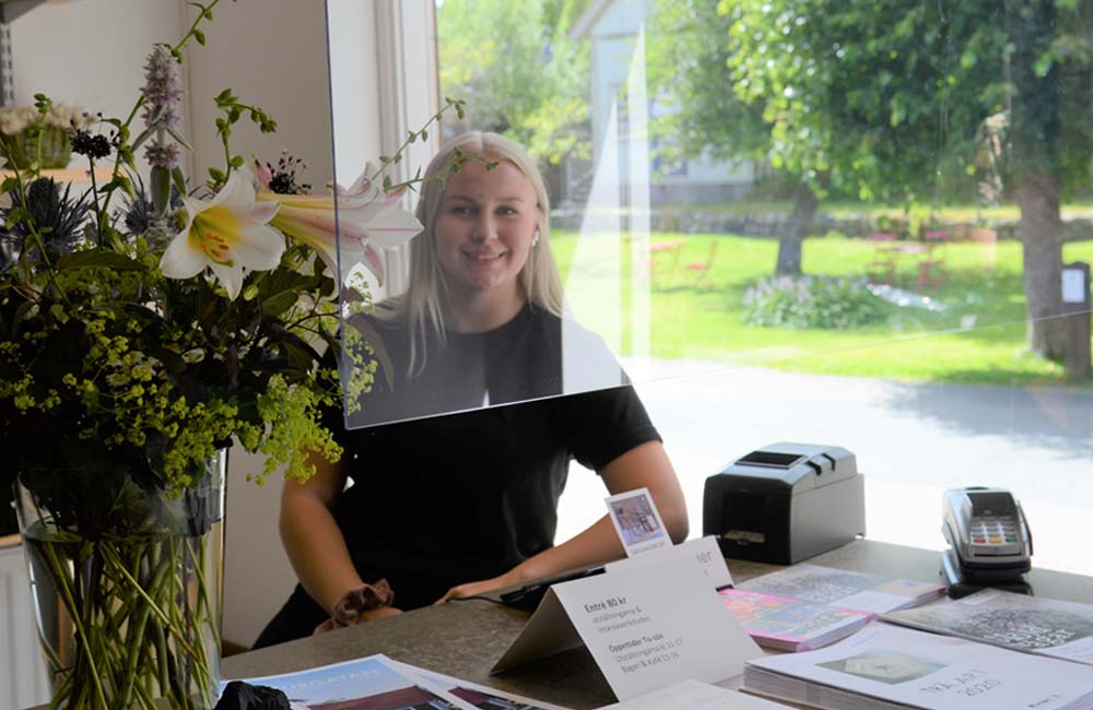 Ung kvinna sittandes i reception med fönster i bakgrunden.