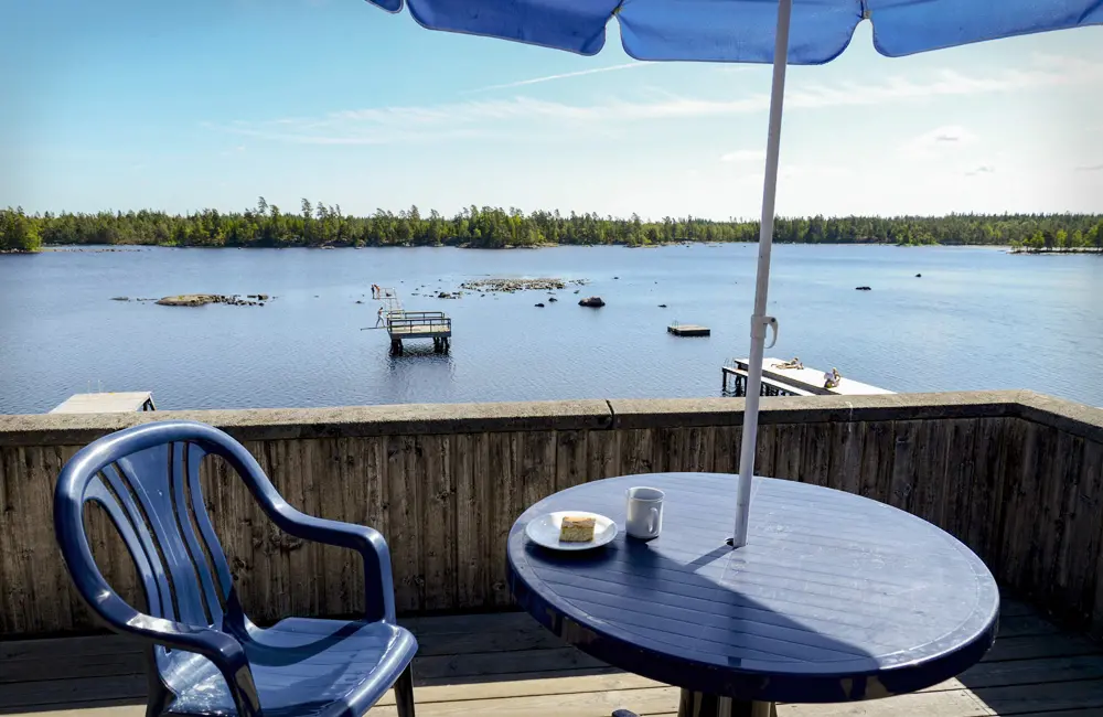 en liten sittplats vid en sjö med blå bord, stol och parasoll. soligt ute.