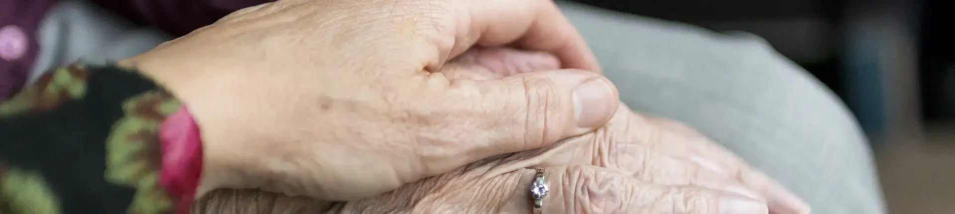 En hand hålls över en rynkig gammal hand.