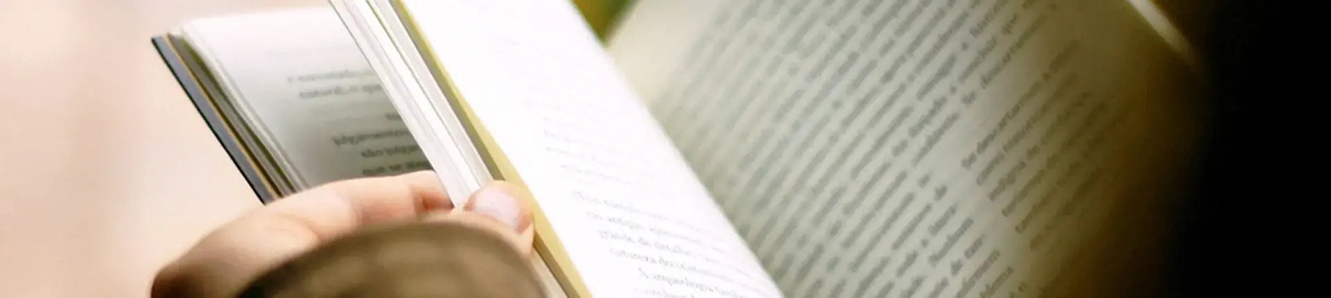 En tumme som bläddrar i en uppslagen bok.