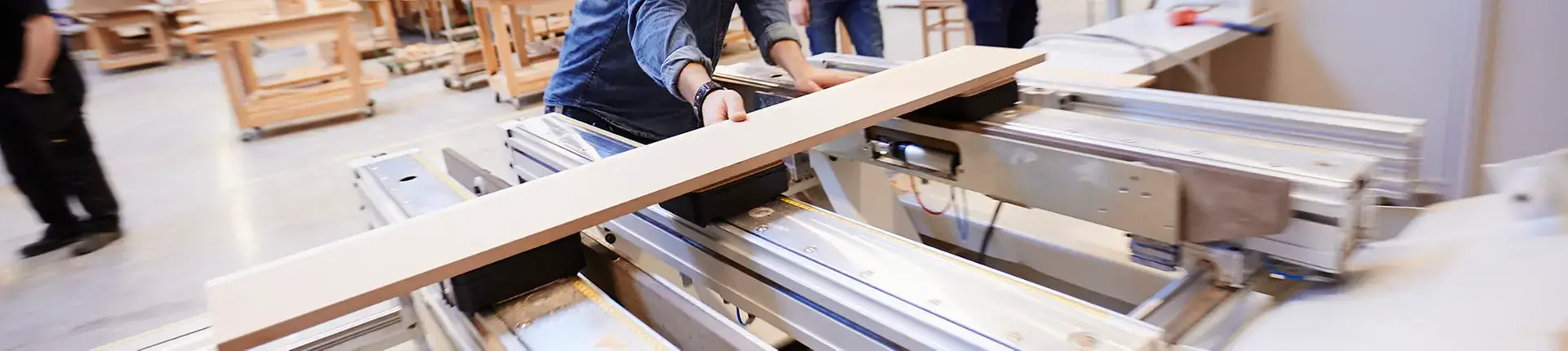 Man ser händerna på en person som lägger en träskiva i en CNC-maskin.