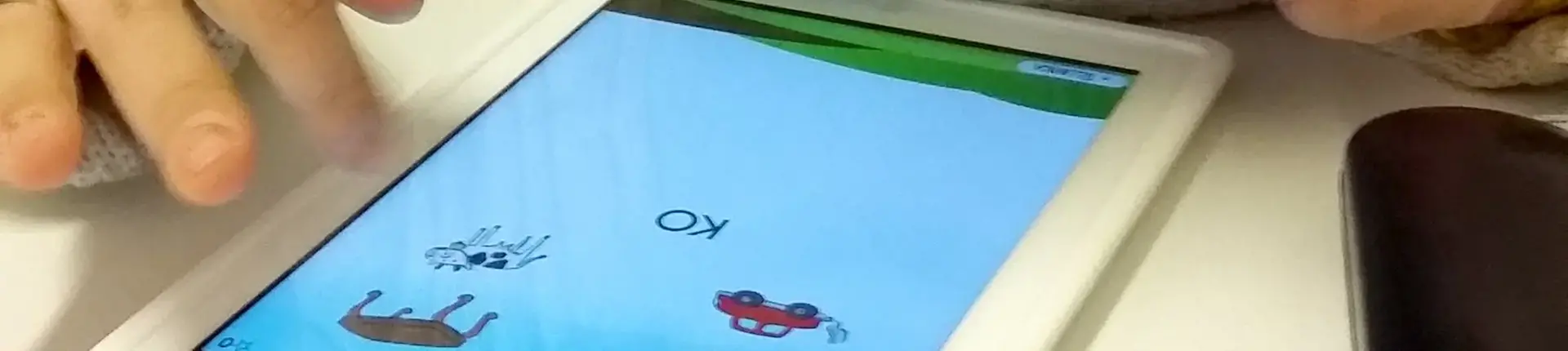 En hand som trycker på en Ipad med korta ord och bilder.
