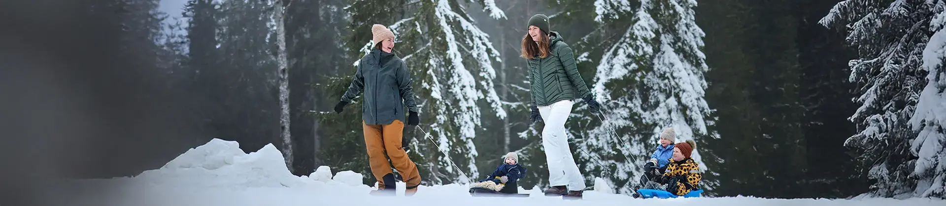 Två kvinnor drar ett par barn på pulka efter sig. 