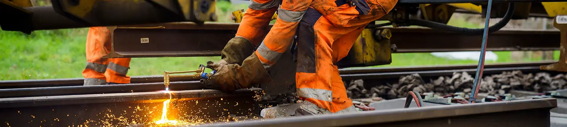 Man i orangea arbetskläder som svetsar på ett järnvägsspår.
