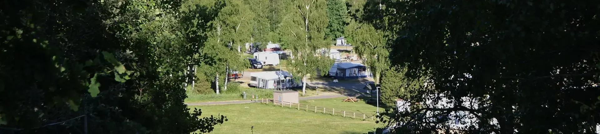 Camping i glänta med husvagnar och kringliggande skog.