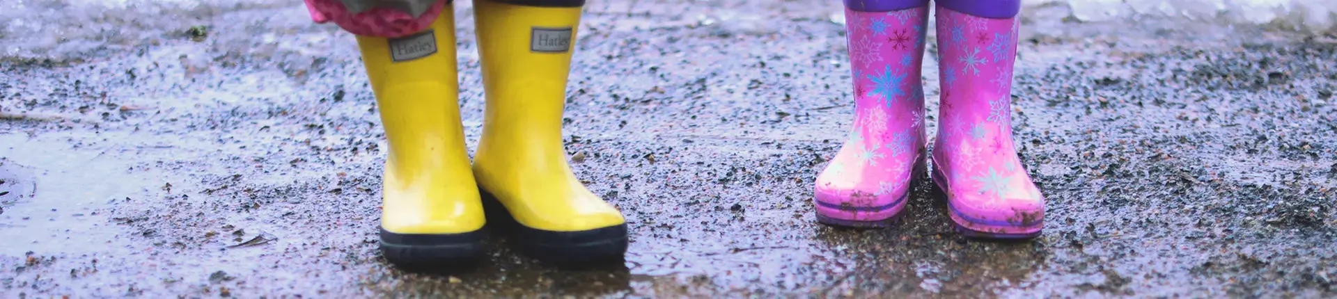 Två barnben och gummistövlar i en vattenpöl.