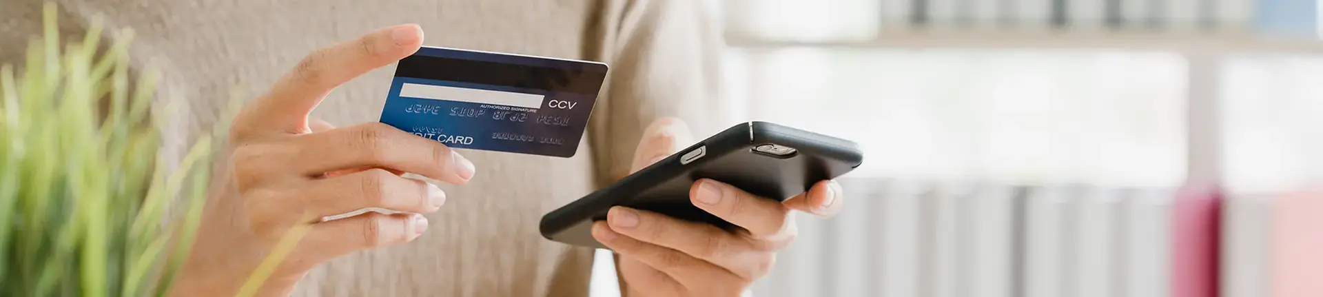 Ung person beställer varor på nätet med mobiltelefon och betalkort i händerna.