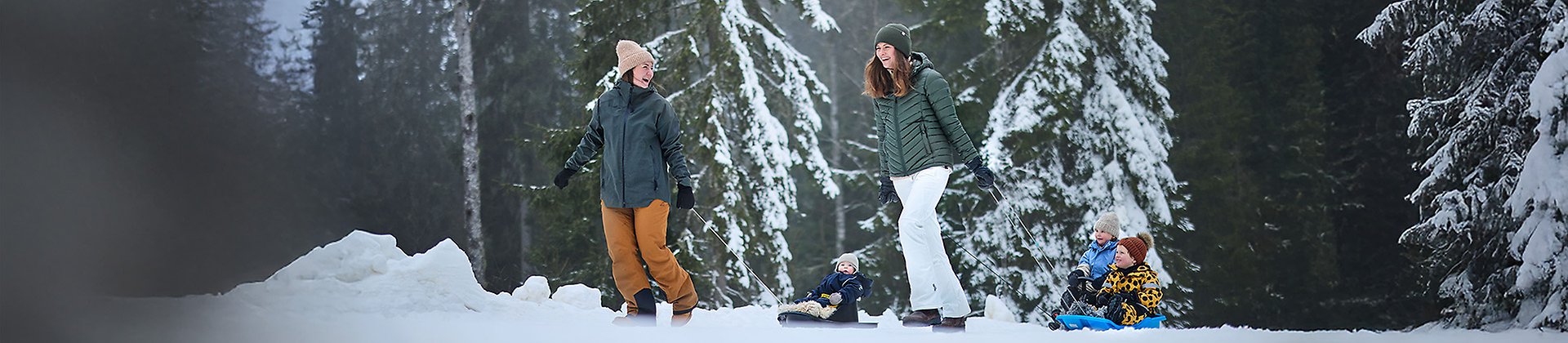 Två kvinnor drar ett par barn på pulka efter sig. 