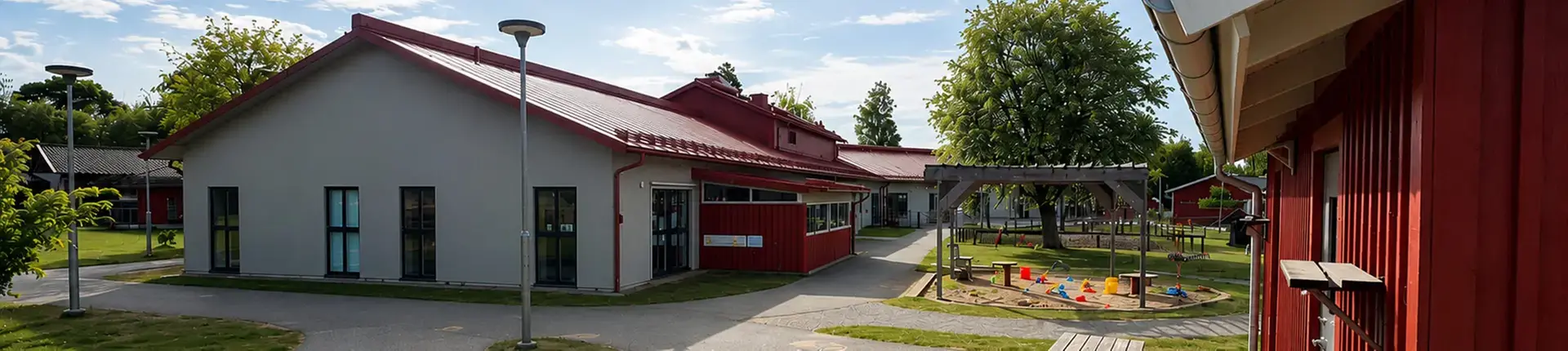 En skolgård med sandlåda, samt ett hus med rött tak och vit putsfasad